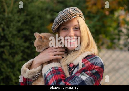 Lächelnde junge Frau mit Erzkatze auf natürlichem Hintergrund. Gemütlicher Herbst. Umarmung des weichen Konzepts. Stockfoto