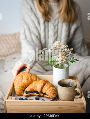 Frühstück im Bett mit frisch gebackenen Croissants mit Blaubeermarmelade und Tee in einer Tasse. Stockfoto