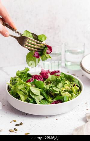 Teller mit Salat und Gläsern, Hände, die Salat im Besteck aufheben Stockfoto