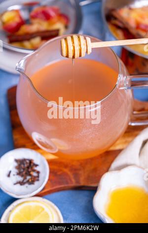 Honig, der in Apfeltee in einer Teekanne tropft, Nelken, Apfelscheiben drum herum. Stockfoto