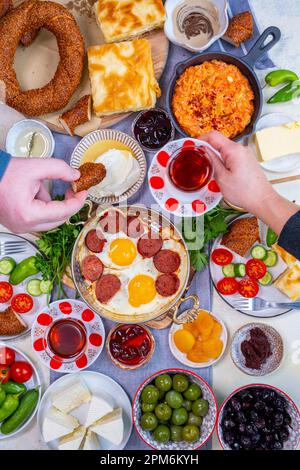 Traditioneller türkischer Frühstückstisch. Eier mit Sujuk, Gemüse, Marmelade, Oliven und Käse. Frau und Mann genießen türkisches Essen und Tee. Stockfoto