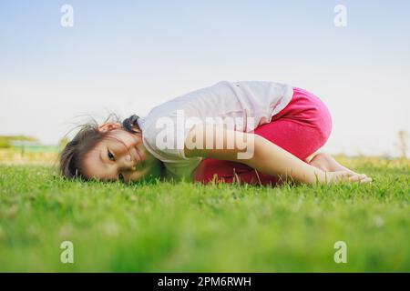 Kindermeditation mit Yoga-Pose auf grünem Grasfeld. Aktivitäten im Freien für Kinder, Yoga-Übungen, Kinder können lernen, wie man trainiert. Stockfoto