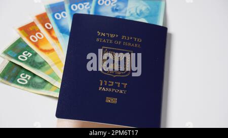 Blauer israelischer Pass (darkon). Pass mit goldenem, biometrischem Schild und bunten israelischen Banknoten Stockfoto