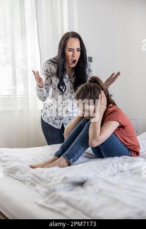 Häusliche, nicht körperliche Gewalt, wenn eine Frau ein junges Mädchen anschreit, das sich die Ohren zudeckt, wenn sie auf einem Bett sitzt. Stockfoto