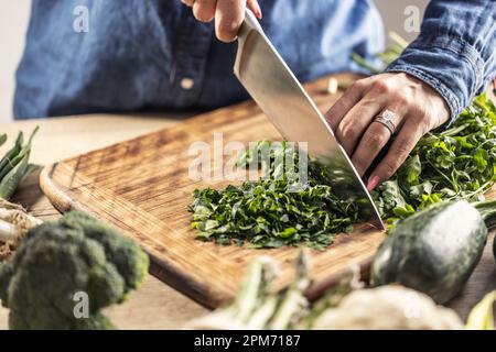 Details weiblicher Hände, die ein Messer halten und frisches Petersilie-Grün hacken. Stockfoto