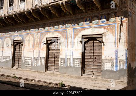 Geschnitzte Holztüren und farbenfrohe Gemälde an der Außenwand eines alten Haveli in Ramgarh, Shekhawati, Rajasthan, Indien Stockfoto