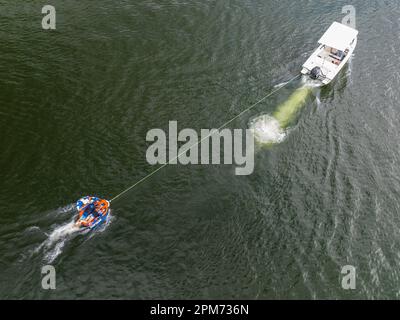 Mackay, Queensland, Australien - April 2023: Drohnenantenne eines Motorboots, das Kinder auf Röhren über den Kinchant Dam schleppt Stockfoto