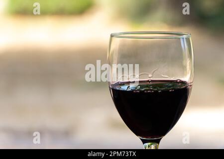 Nahaufnahme eines Rotweinglases, gefüllt mit Weintränken, die dem verschwommenen Hintergrund einen Hauch von Eleganz verleihen. Ein luxuriöses und raffiniertes Image Stockfoto