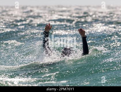 Ein Taucher in Not signalisiert im Meer mit Armen in der Luft, um Hilfe bei einer Rettungsübung für Taucher zu signalisieren Stockfoto