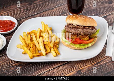 Köstlicher gegrillter Burger auf weißem Teller auf einem Holztisch. Mit Saucen und pommes frites Stockfoto