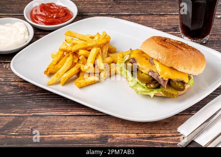 Köstlicher Rindfleischburger mit pommes Frites, Zwiebelringen und Saucen Stockfoto