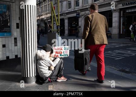 Ein Mann mit roten Hosen kommt am 4. April 2023 in London, England, an einem Straßenbettler in der Nähe der Liverpool Street Station in der City of London vorbei, auch bekannt als The Square Mile, dem Finanzviertel der Hauptstadt. Stockfoto