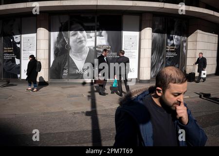 Fußgänger laufen am 4. April 2023 in London, England, an einer großen Plakatwand einer geschlossenen Zweigstelle von M&S (Marks and Spencer) auf Bishopsgate in der City of London, auch bekannt als The Square Mile, vorbei. Stockfoto