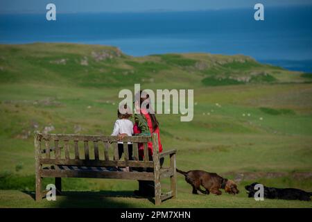 Mutter und Kind auf einer Bank mit Cocker Spaniel-Hunden, die vom Glengorm Castle in der Nähe von Tobermory, Isle of Mull, Schottland, Großbritannien, auf das Meer blicken Stockfoto