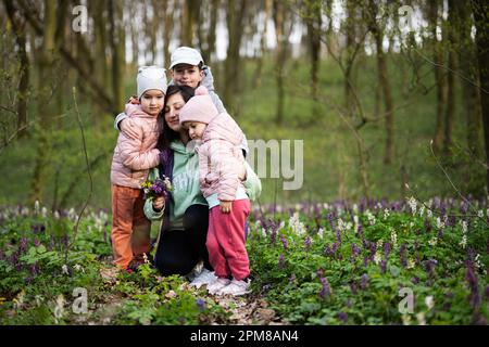 Alles gute zum Muttertag. Wir lieben dich, mom. Mutter mit einem Blumenstrauß und drei Kindern im blühenden Frühlingswald. Stockfoto