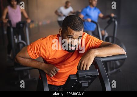 Ein bärtiger junger Mann, der im Fitnessstudio mit dem Fahrrad fährt Stockfoto