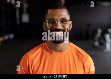 Porträt eines lächelnden bärtigen, birassischen jungen Mannes mit Brille im Fitnessstudio Stockfoto