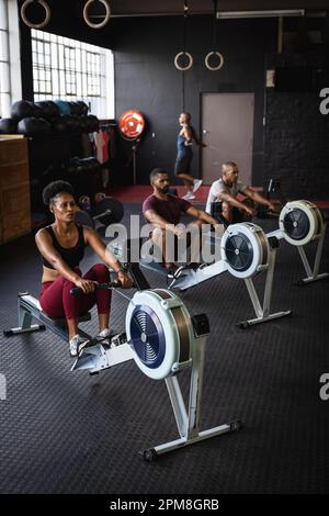 Blick aus der Vogelperspektive auf birassische junge Männer und Frauen, die auf Rudergeräten im Fitnessstudio trainieren, Kopierbereich Stockfoto