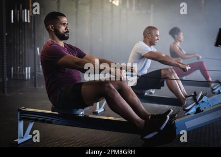 Seitenansicht eines birassischen jungen Mannes und einer Frau, die auf Rudergeräten im Fitnessstudio trainieren, Kopierraum Stockfoto