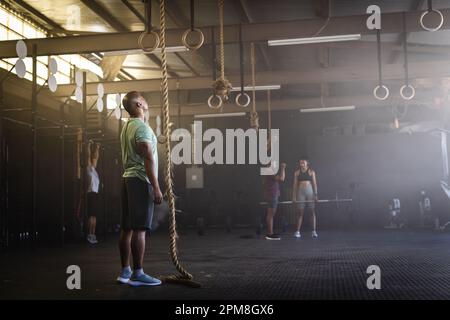 Seitenansicht eines birassischen jungen Mannes, der auf ein Seil schaut, während er im Fitnessstudio steht, Kopierraum Stockfoto