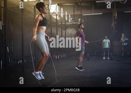 Seitenansicht eines birassischen jungen Mannes und einer Frau, die mit einem Seil im Fitnessstudio springen, Kopierraum Stockfoto