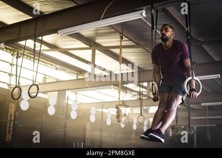 Ein bärtiger junger Mann, der im Fitnessstudio an Turnringen hängt Stockfoto