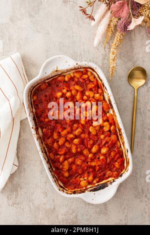 Gesundes Frühstück und Mittagessen, gedünstete weiße Bohnen mit Karotten, Zwiebeln und Tomaten, Blick von oben auf eine ovale Keramikrösterei mit gedünsteten Hülsenfrüchten Stockfoto