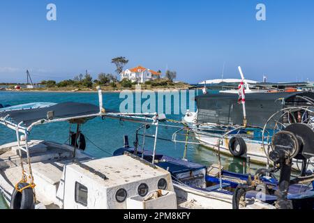 Zwei Fischerboote liegen eng aneinandergeschlossen im Fischereihafen von Famagusta, Türkische Republik Nordzypern (TRNC). Zwischen ihnen erhebt sich auf einer kleinen Landzunge die weiße Villa im britischen Kolonialstil mit ihrem rotgedeckten Dach. Stockfoto