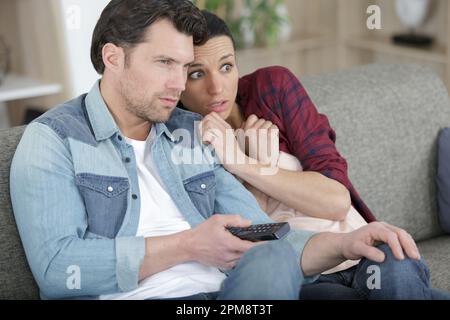 Ein Paar, das auf der Couch sitzt und sich einen Horrorfilm ansieht Stockfoto
