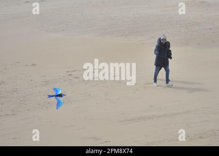 Storm Noa, Boscombe, Bournemouth, Dorset, Vereinigtes Königreich, 12. April 2023, Wetter. Ein Mann, der am Morgen bei starkem Wind und stürmischen Bedingungen am Strand einen Drachen fliegt. Kredit: Paul Biggins/Alamy Live News Stockfoto