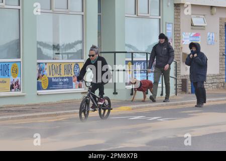 Storm Noa, Boscombe, Bournemouth, Dorset, Vereinigtes Königreich, 12. April 2023, Wetter. Mann auf einem Fahrrad auf Hundegängern auf der Promenade bei starkem Wind und stürmischen Bedingungen am Meer am Morgen. Kredit: Paul Biggins/Alamy Live News Stockfoto