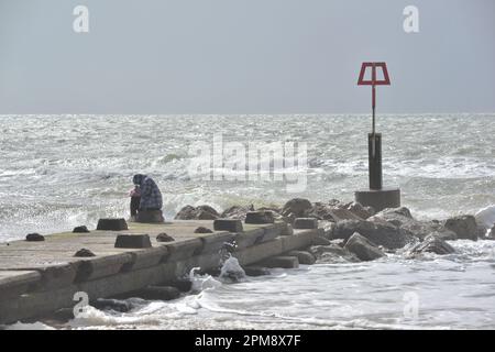 Storm Noa, Boscombe, Bournemouth, Dorset, Vereinigtes Königreich, 12. April 2023, Wetter. Mann sitzt am Strand groyne bei starkem Wind und stürmischen Bedingungen am Meer am Morgen. Kredit: Paul Biggins/Alamy Live News Stockfoto