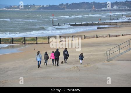 Storm Noa, Boscombe, Bournemouth, Dorset, Vereinigtes Königreich, 12. April 2023, Wetter. Spaziergang in einer Familiengruppe am Strand bei starkem Wind und stürmischen Bedingungen am Meer am Morgen. Kredit: Paul Biggins/Alamy Live News Stockfoto