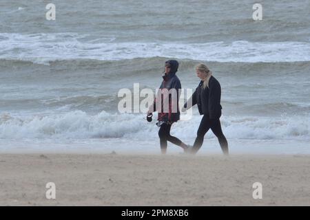 Storm Noa, Boscombe, Bournemouth, Dorset, Vereinigtes Königreich, 12. April 2023, Wetter. Zwei junge Frauen, die morgens am Strand spazieren, haben starke Winde und stürmische Bedingungen am Meer. Kredit: Paul Biggins/Alamy Live News Stockfoto