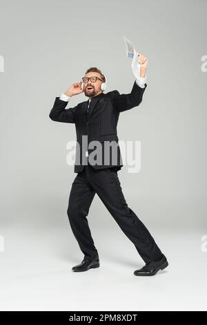 Ein Geschäftsmann mit Brille, der Musik hört und singt, während er die Kopfhörer auf einem grauen Stockbild hält Stockfoto