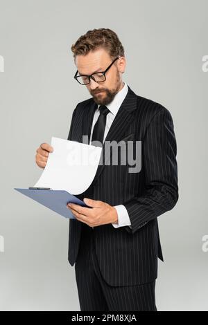 Gut gekleideter Geschäftsmann mit Brille, der Klemmbrett und Papier isoliert auf grauem Stockbild hielt Stockfoto