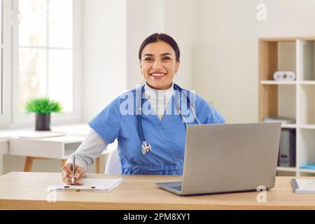 Porträt einer fröhlichen jungen, freundlichen Ärztin in blauer medizinischer Uniform, die in die Kamera schaut. Stockfoto
