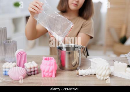 Arbeits- und Hobby-Konzept - junge Frau, die zu Hause Kerzen macht, Sojawachs in die Pfanne gießt Stockfoto