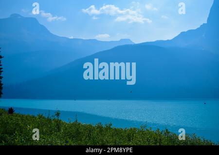 Ein wunderschöner See mit blauem Wasser und die Kanadischen Rocky Mountains im Hintergrund an einem sonnigen, aber trüben Sommertag. Stockfoto