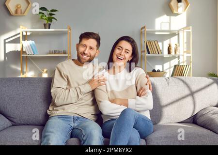 Junges, glückliches Ehepaar, das auf dem Sofa im Wohnzimmer sitzt und lacht. Stockfoto