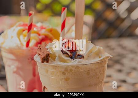 Köstliche Sommermilchshake-Getränke mit Obst, Schokolade und cremiger Sahne mit gestreiften Strohhalmen. Stockfoto