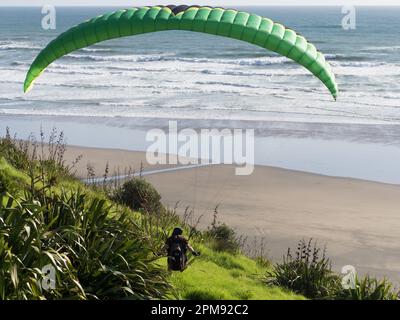 Ein Gleitschirm bereitet sich auf den Start auf einem grünen Hügel mit Strand und Meer im Hintergrund vor. Hinterleuchtete Silhouette. Sport. Erholung Stockfoto