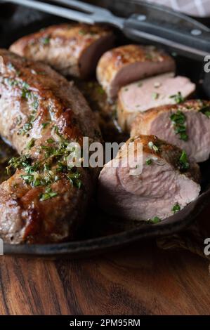 In der Pfanne gebratenes mittelgroßes Schweinefilet mit geschmolzener Kräuterbutter in einer gusseisernen Pfanne. Stockfoto