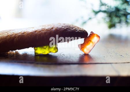 Gummibären, die mit einem Keks auf einem Esstisch spielen. Stockfoto