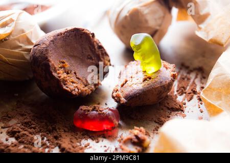 Gummibärchen, die mit einem Schokoladenball auf einem Esstisch spielen. Stockfoto