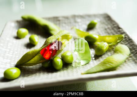 Gummibären, die mit Edamamabohnen auf einem Esstisch spielen. Stockfoto