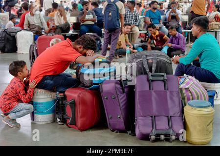 Ein verspielter indischer Junge, der seinen schlafenden Vater ärgert, ihre Familie am Chhatrapati Shivaji Maharaj Terminus in Mumbai, Indien, und auf ihren Zug wartet Stockfoto