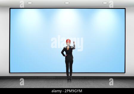 Eine Frau mit Helm, die auf eine große Tafel zeichnet Stockfoto