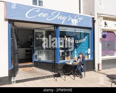 Reife Frau sitzt vor CEE Jays Café in Front Street, Newbiggin by the Sea, Northumberland, England, Großbritannien Stockfoto