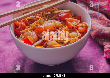 Schüssel mit Garnelen unter Rühren anbraten, wobei die Stäbchen auf der Schüssel ruhen. Stockfoto